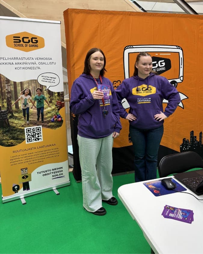 Two of the School of Gaming team in purple School of Gaming hoodies at an event stand